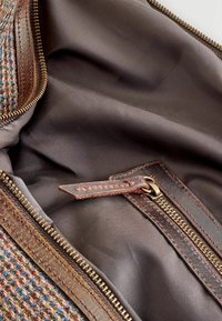 Textured fabric bag with a brown leather zipper, featuring a contrasting interior in dark brown. Includes a leather zipper pull detail.
