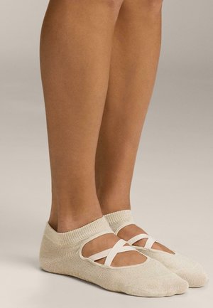 Chaussettes de danse beige clair en tissu texturé avec des bretelles élastiques croisées et une coupe basse, exposant la cheville et le pied.