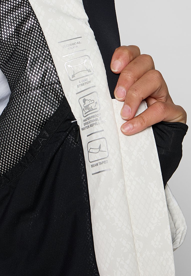 Schwarzer Mesh-Stoff mit weißem strukturiertem Überzug, der Pflegehinweise zeigt. Bemerkenswerte Details sind die Nahtversiegelung und die Kennzeichnung für Vier-Wege-Stretch.