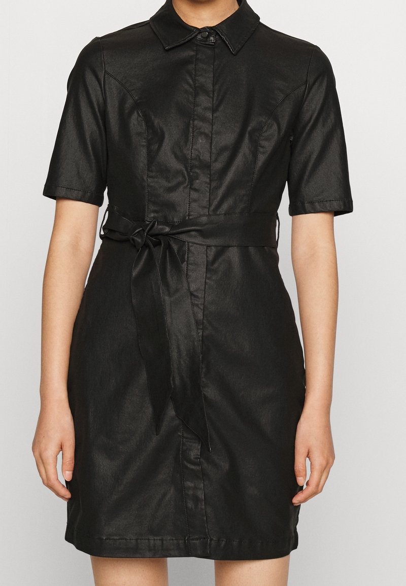 Czarna krótka sukienka z gładkiego materiału, z kołnierzykiem, z zapinaniem na guziki z przodu i wąskim paskiem w talii.