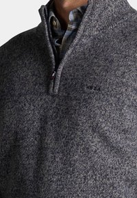 Pullover trui van donkergrijze gebreide stof met een kwart-rits kraag en een subtiele gemêleerde textuur. Heeft een logo op de borst.