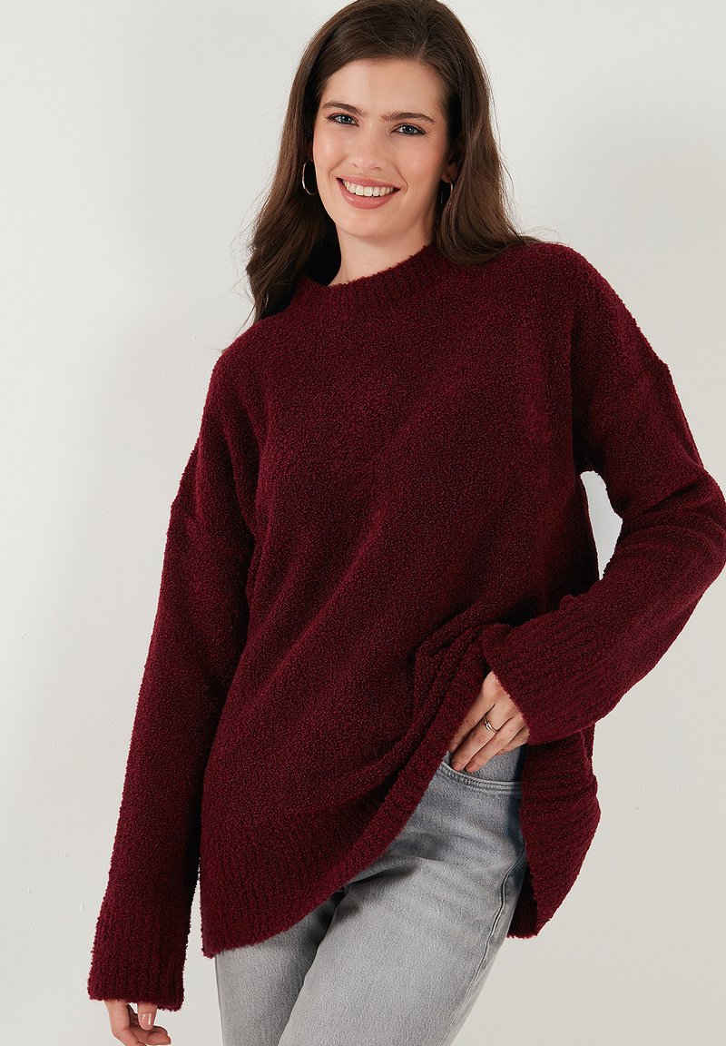 Burgundy knit sweater with a textured finish, featuring a round neckline and long sleeves, paired with light gray jeans.
