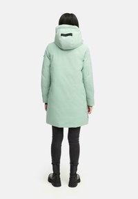 Lys grøn, hættefyldt vinterparka med et strømlinet design. Har et logo på ryggen, forlommer og en længde til midten af lårene.