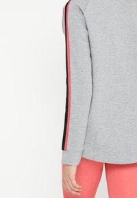 Sudadera deportiva gris de manga larga, con franjas laterales en negro y rosa. Tela suave y texturizada, corte holgado y cuello redondo.