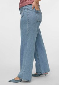 Jeans de mezclilla de piernas anchas en azul claro, con cintura alta, bolsillos traseros y dobladillos sin terminar. Combinados con tacones de punta en azul claro.