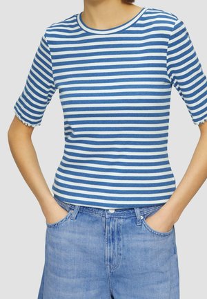 Osoba ubrana w krótki rękaw w niebiesko-białe poziome paski i jasnoniebieskie dżinsy z rękami w kieszeniach.