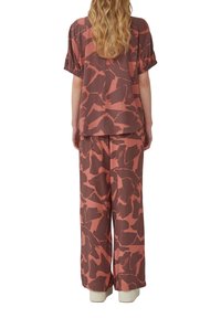 Twee-delige outfit met een T-shirt met korte mouwen en een broek met wijde pijpen, voorzien van een abstracte bruine en roze patroon, gemaakt van lichte stof.