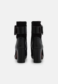 Bottines noires présentant un motif texturé peau de serpent, une finition en suède, des talons épais carrés et une large sangle à boucle autour de la cheville.