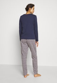 Haut à manches longues bleu marine associé à un pantalon de pyjama à motifs présentant un design en chevron noir et blanc. Tissu doux et décontracté avec des poignets élastiques.