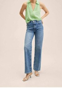 Chemise sans manches vert clair avec col et motif en losanges, associée à un jean bleu taille haute à coupe droite et des sandales blanches à talons.