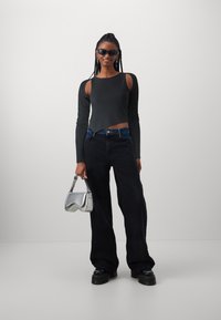 Must mustriba pika varrukaga crop top mustade külje lõigetega, kombineeritud vabalt istuvate mustade teksadega. Mudel hoiab käes metalset hõbedast käekotti.