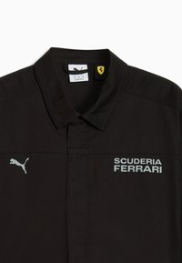 Sort kortærmet skjorte med klassisk krave, prydet med sølvfarvet "SCUDERIA FERRARI" tekst og Puma-logo. Inkluderer et gult Ferrari-mærke.