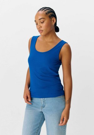 Camiseta de tirantes azul con escote redondeado y tirantes anchos, combinada con jeans de color azul claro, llevada por una persona con cabello trenzado.