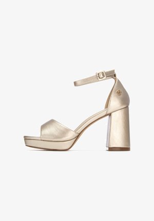 Sandalia metálica dorada de tacón alto con puntera abierta, correa en el tobillo y tacón grueso. Textura suave y diseño minimalista.