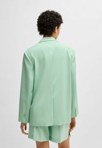 Blazer verde menta con una vestibilità rilassata, design a un petto, colletto affilato e polsini abbottonati. Abbinato a pantaloni corti dello stesso colore.