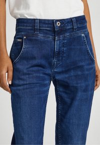 Tmavě modré džíny z denimu s klasickým designem pěti kapes, s předním zapínáním na knoflík a jemnými detaily prošívání.