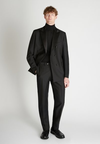 Schwarzer, maßgeschneiderter Anzug mit einer doppelt geknöpften Jacke und schmal geschnittenen Hosen, kombiniert mit einem schwarzen Rollkragenpullover. Glatte Textur, minimalistisches Design.