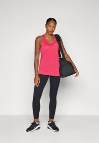 Top sportivo rosa, leggings neri, sneakers neri e una borsa nera. Il top presenta un logo, una vestibilità aderente e una texture morbida.