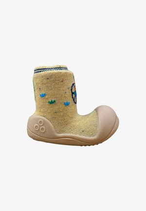 Zapato de bebé beige suave con suela de goma flexible y parte superior tipo calcetín de punto amarillo decorada con pequeños patrones de flores azules y verdes.