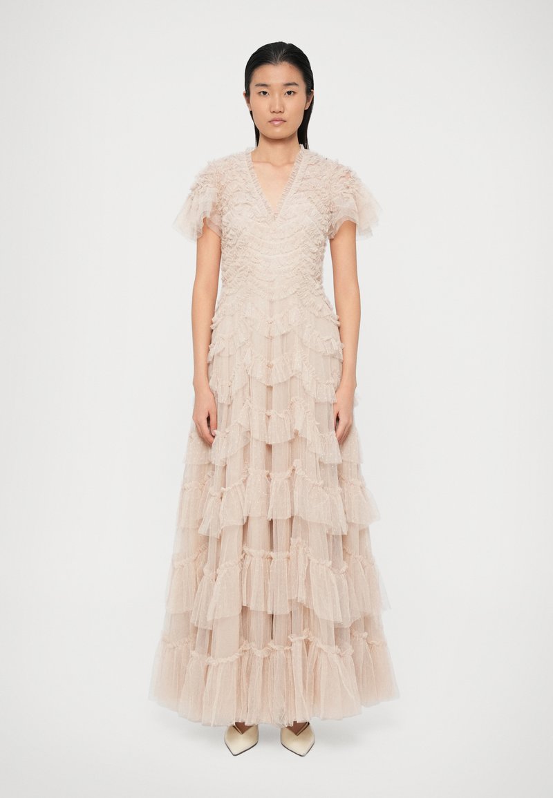 Μακριά, πολυεπίπεδη φορεσιά από απαλό ροζ τούλι με βολάν, βαθύ V ντεκολτέ και κοντά φουσκωτά μανίκια. Η φούστα φτάνει μέχρι το δάπεδο, προσφέροντας υφή στην εμφάνιση.