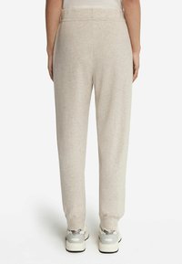 Ljust beige sweatpants i mjukt tyg, med avslappnad passform och avsmalnande ben. Bärs med grå och vita gymnastikskor.