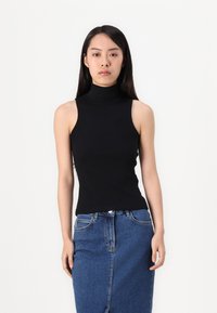 Svart ermela topp med høy hals laget av glatt stoff, sammen med et denimskjørt. Antrekket har en tettsittende design og minimale detaljer.