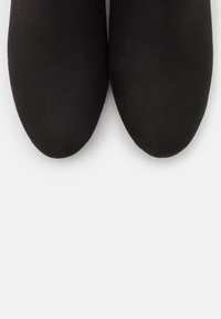 Paire de bottines en daim noir à bouts arrondis sur un fond clair uni.