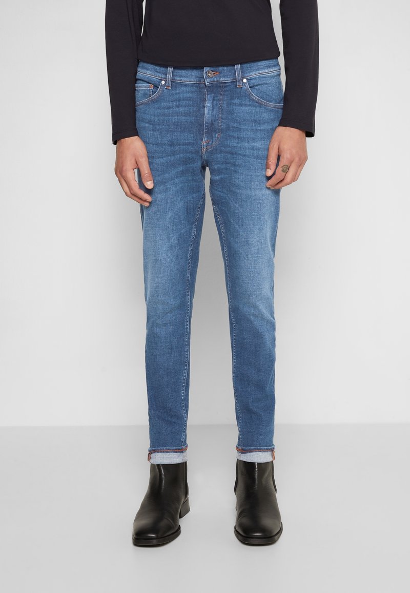 Modré džínové kalhoty slim fit s pěti kapsami, s jemným blednutím a kontrastním prošíváním na kapsách a manžetách.