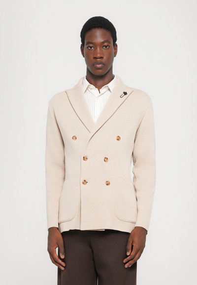 Beige Doppelreiher-Blazer aus strukturiertem Stoff mit großen braunen Knöpfen, Schalkragen und aufgesetzten Taschen. Schwarze Akzentnadel inklusive.