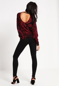 Maglione rosso e nero a fantasia con schiena scoperta, abbinato a jeans skinny neri e sandali con tacco nero.