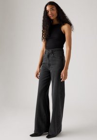 Jeans noirs taille haute avec une coupe évasée et un design classique à cinq poches, associés à un débardeur noir en maille côtelée.