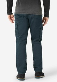 Dark teal cargo pants with multiple side pockets, elastic cuffs, and a relaxed fit. The fabric appears durable and slightly textured.