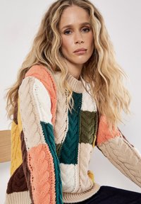 Sweter dzianinowy z wzorami w warkocze w blokach pomarańczowym, zielonym, beżowym, żółtym, brązowym i białym. Żebrowany dekolt i mankiety, teksturowane wykończenie.