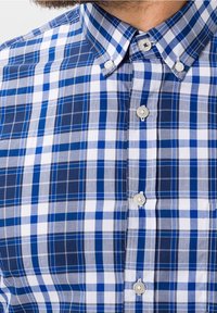 Bavlněná košile s modro-bílým kostičkovaným vzorem, vybavená límcem na knoflíčky a knoflíky po celé přední části. Hladká textura.