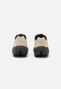Baskets en daim beige avec semelles en caoutchouc noir. Présentent des accents cousus et le logo au niveau du talon. Doublure textile pour le confort.
