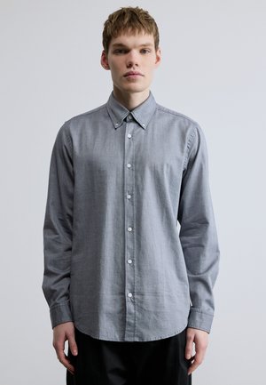 Grau karierte Hemdjacke mit subtiler Textur, langen Ärmeln und spitzem Kragen. Ausstattung mit weißen Knöpfen und einem geschwungenen Saum.