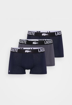 Ensemble de slips boxers pour homme en bleu marine et gris. Tissu doux avec ceintures élastiques arborant le logo Lacoste. Trois paires exposées.