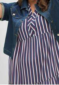 Jeansjacka över en marinblå och vitrandig klänning med röda detaljer, med veckad nederdel och V-ringning.