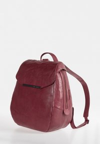 Leder-Rucksack in tiefem Burgunderrot mit Klappenverschluss, einem Reißverschluss und verstellbaren Trägern. Glatte Textur mit dezentem Branding-Detail.