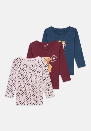 Tres camisas infantiles de manga larga: rosa con lunares negros, granate con un diseño de corazón de osito de peluche y azul con una ilustración de dos niños.
