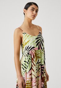 Rochie cu model floral cu desene de frunze verzi, roz și negre. Bretele subțiri se atașează cu un element circular. Croială fluidă, potrivită liber.