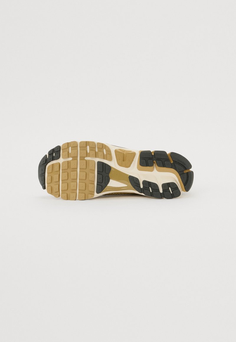 Schuhsohle mit einem gemusterten Design aus schwarzem und braunem Gummi, strukturiert für besseren Grip, und einer weißen Zwischensohle zur Dämpfung.