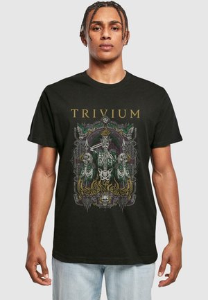 Mann iført svart "TRIVIUM" T-skjorte med detaljert grafikk av skjelettfigurer, flammer og intrikat dekorativ ramme.