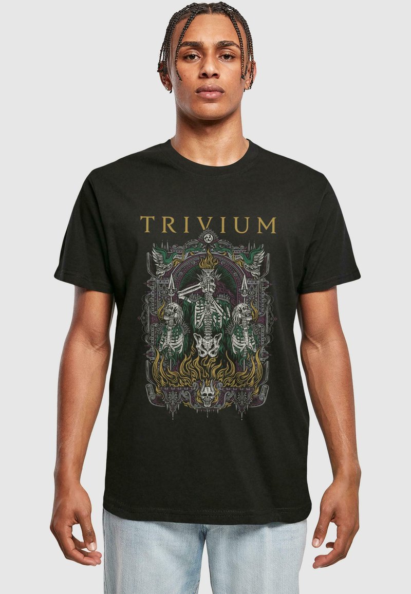 Homme portant un T-shirt noir "TRIVIUM" avec un graphisme détaillé de figures squelettiques, de flammes et d'un cadre décoratif intricé.