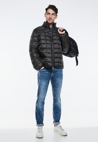 Černá péřová bunda s prošívaným vzorem, se zipem a vysokým límcem; nošena s světle modrými džíny a bílými teniskami.