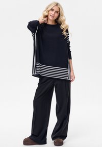 Czarny, dziany, oversize'owy sweter z białymi, poziomymi paskami na dole, w połączeniu z szerokimi, czarnymi spodniami o luźnym kroju i miękkiej fakturze.