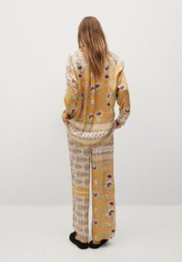 Blouse à motifs jaunes et pantalon ample avec imprimés floraux ; tissu doux, coupe décontractée, finitions détaillées et accents de couleurs contrastées.