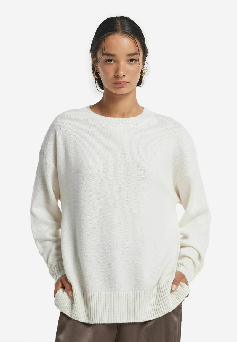 Übergroßer weißer Strickpullover mit rundem Ausschnitt, gerippten Bündchen und Saum; verfügt über eine strukturierte Oberfläche und seitliche Taschen.