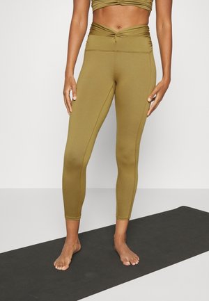 Leggings taille haute vert olive avec un détail torsadé à l'avant, fabriqués en tissu extensible. Texture lisse, coupe ajustée, longueur cheville.