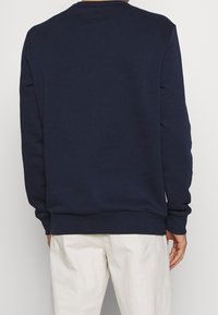 Felpa blu navy con maniche lunghe, collo rotondo, polsini e orlo a coste, realizzata in un tessuto morbido, con minimi dettagli di cucitura.